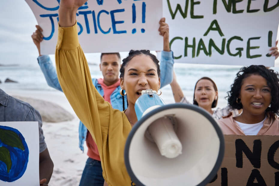 Social justice activists protesting outside, holding signs and microphones, with their fists raised in solidarity, advocating for change and equality.