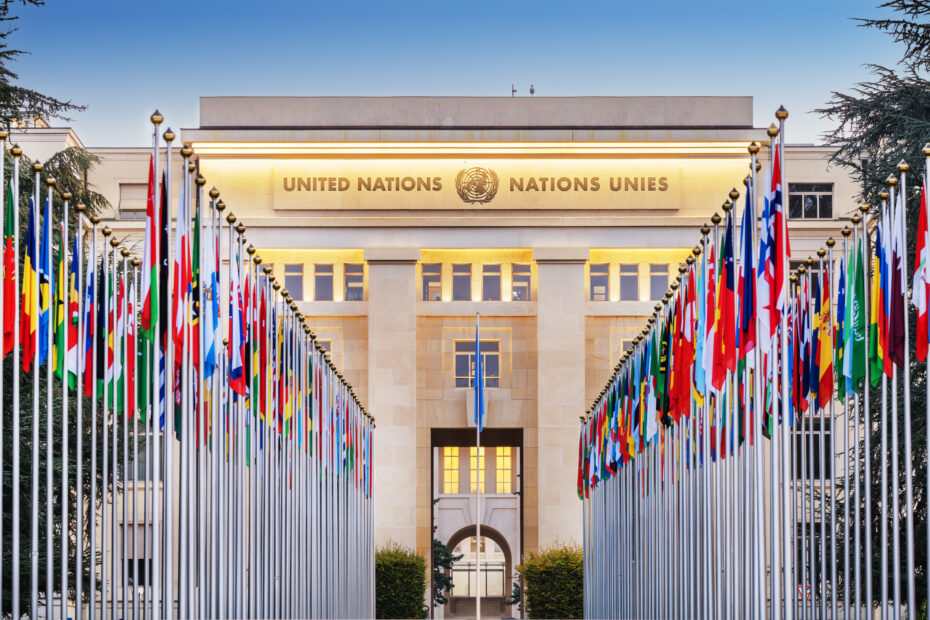 A photo of the Palais des Nations in Geneva, Switzerland, with the flags of all United Nations member states displayed in front, symbolizing global cooperation and diplomacy