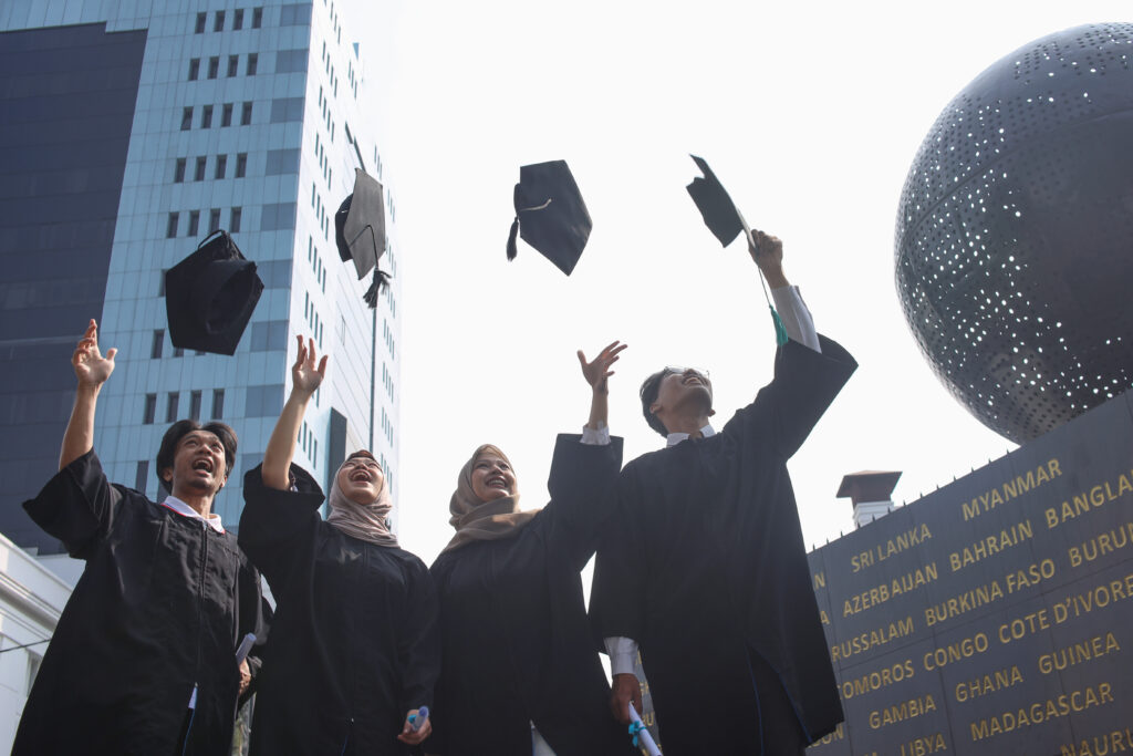 Happy smiling asian graduate students from university throwing their caps in the air